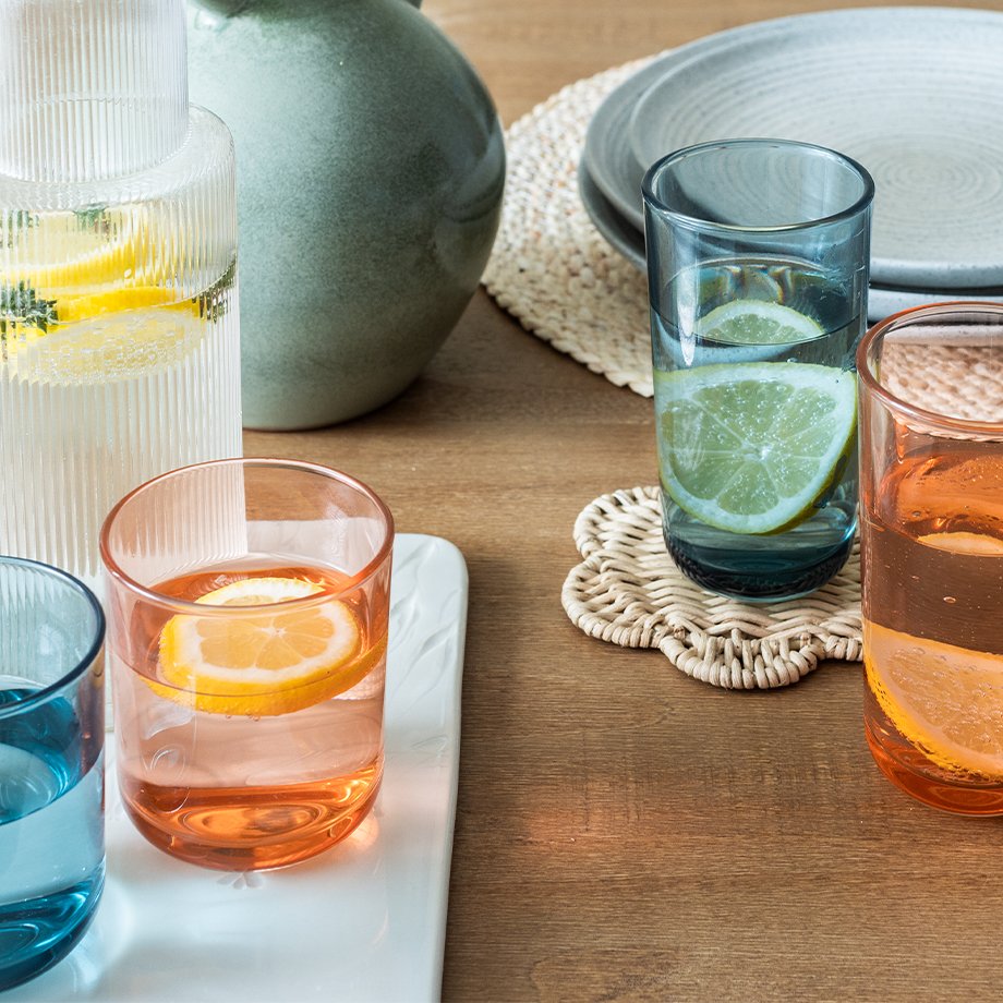 A summer dining tbale set up with wicker scalloped placemats, stone effect tablewear and colourful glassware.
